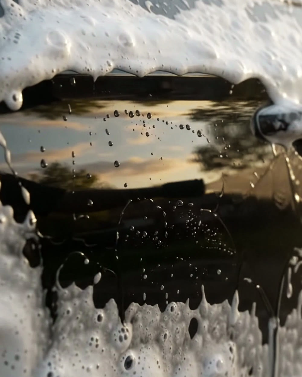Pressure washer jet rinsing thick foam off a black car